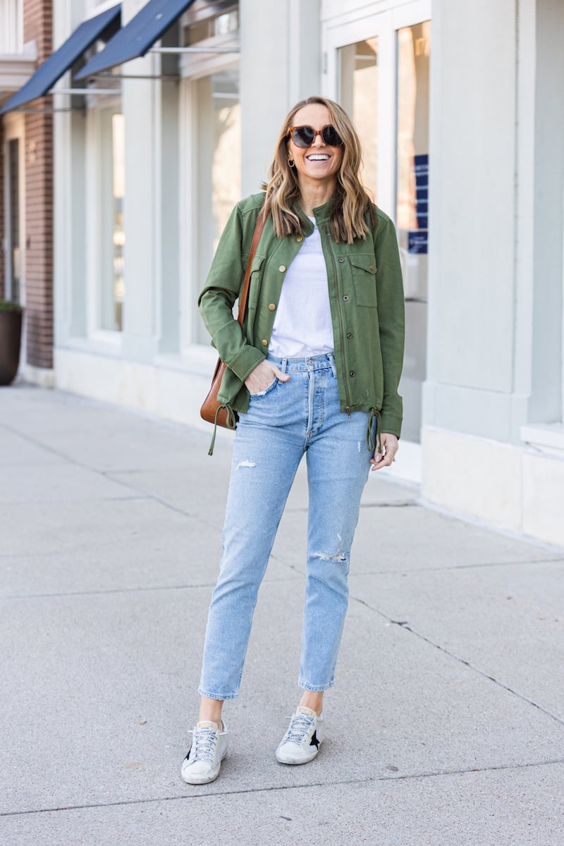 green jacket with lightwash jeans and golden goose sneakers